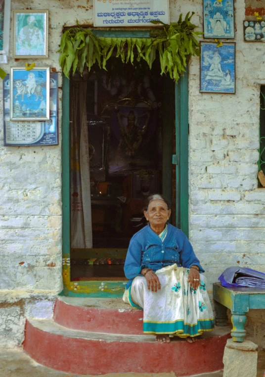 a woman sitting on the steps of a building, kerala village, elderly greek goddess, shop front, square