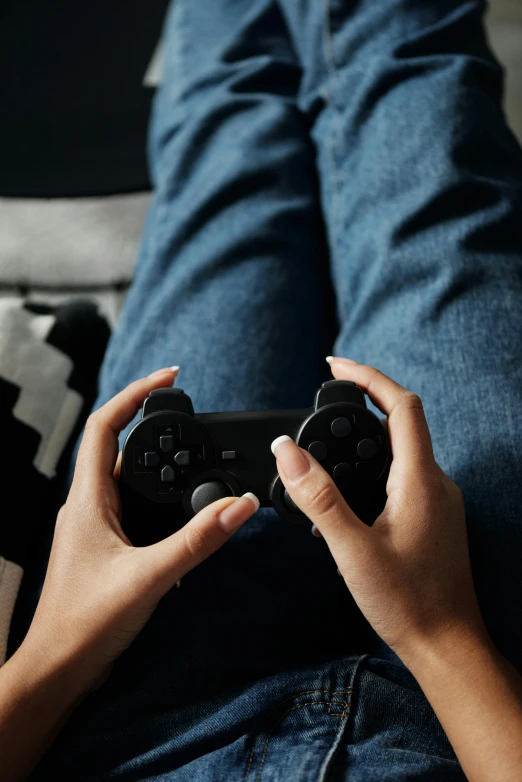 a person sitting on a couch holding a video game controller, wearing a dark shirt and jeans, laying down with wrists together, #trending, square enix