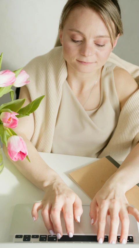 a woman sitting at a table typing on a laptop, an album cover, pexels, romanticism, tulip, low quality photo, folded arms, sitting with flowers