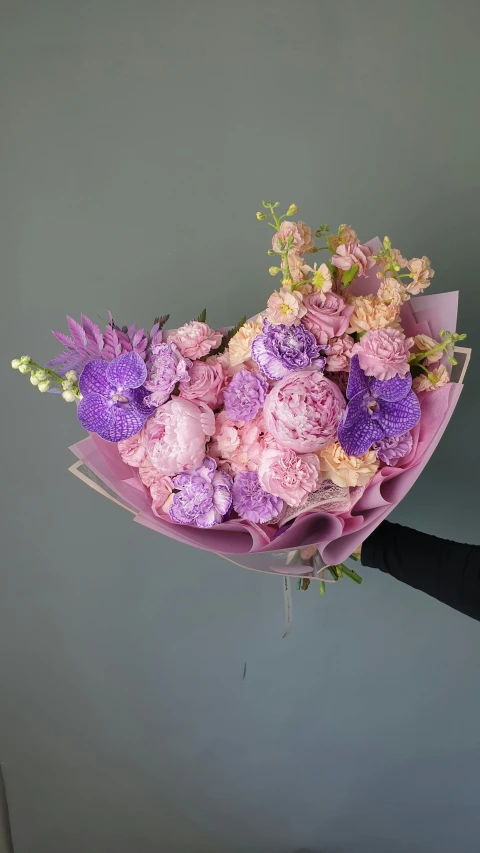 a person holding a bunch of flowers in their hand, purple and pink, lots of pastel colour, from side, floral explosion