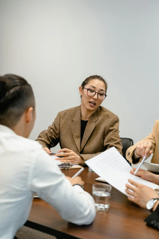a group of people sitting around a wooden table, woman in business suit, thumbnail, david luong, in a meeting room