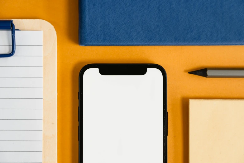 a cell phone sitting on top of a desk next to a notebook, postminimalism, orange backgorund, square shapes, background image, iphone 12