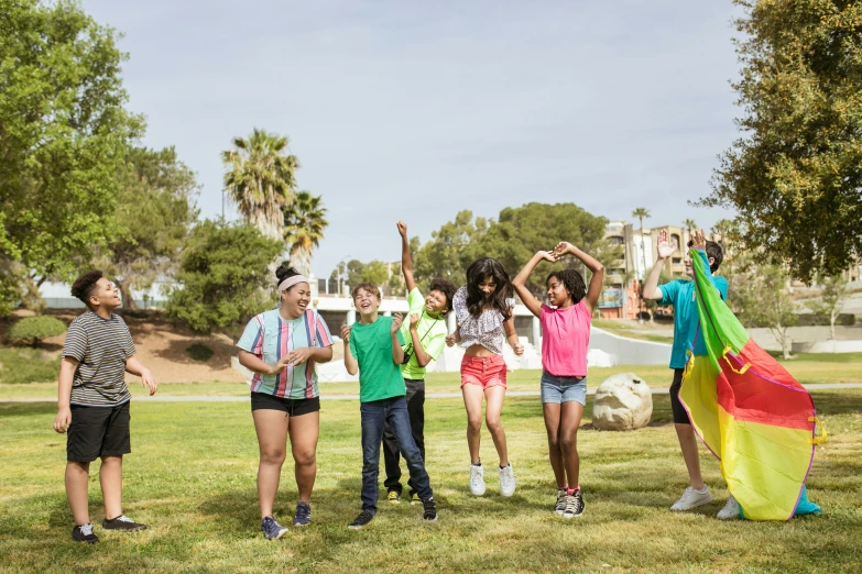 a group of young people standing on top of a lush green field, colourful clothes, los angelos, casual playrix games, cheering