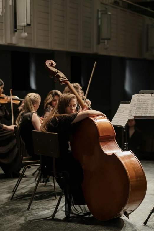 a group of people playing instruments in a room, cello, against a deep black background, university, thumbnail