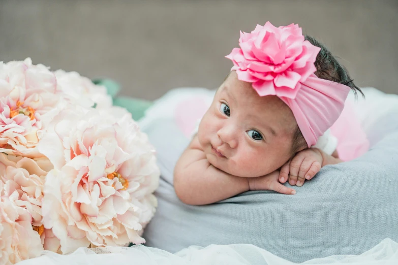 a baby laying on a blanket next to a bunch of flowers, pink headband, louise zhang, mixed race, portrait image