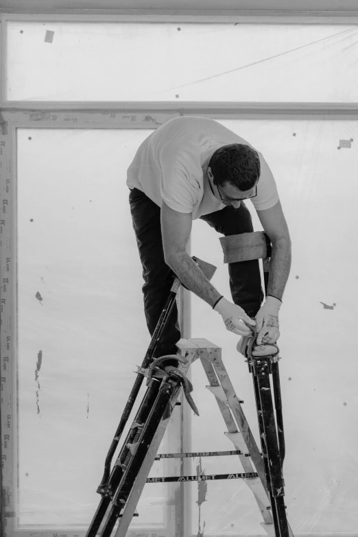 a black and white photo of a man on a ladder, repairing the other one, amr elshamy, knee, glazing
