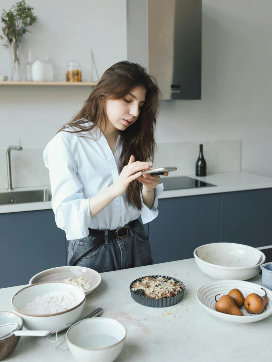 a woman standing in a kitchen looking at her cell phone, trending on unsplash, renaissance, baking a cake, girl with brown hair, low quality photo, grey