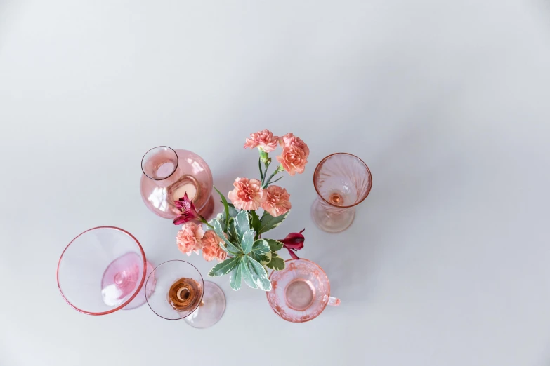 a vase filled with pink flowers sitting on top of a table, by Carey Morris, trending on unsplash, visual art, amber glasses, cups and balls, set against a white background, wide high angle view