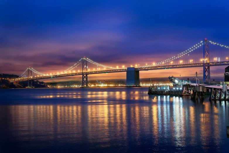 a bridge over a body of water at night, pexels contest winner, city bay bridge aqueduct, golden and blue hour, a colorful, sf