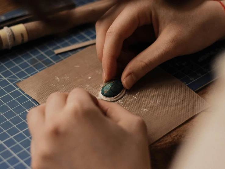 a close up of a person working on a piece of paper, an etching, trending on pexels, arts and crafts movement, copper and emerald inlay, leather, carved soap, thumbnail