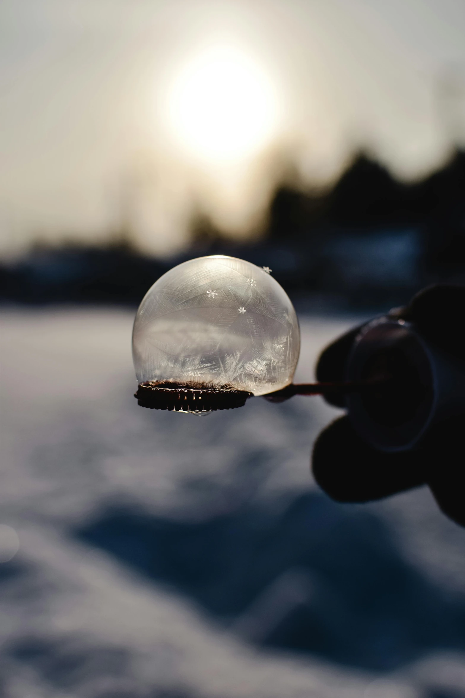 a person holding a bubble in the snow, by Jesper Knudsen, pexels contest winner, fan favorite, sun down, water droplet, inside a marble