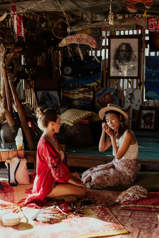 a couple of women sitting on top of a floor, crafts and souvenirs, vibrant aesthetic, boho style, on an island