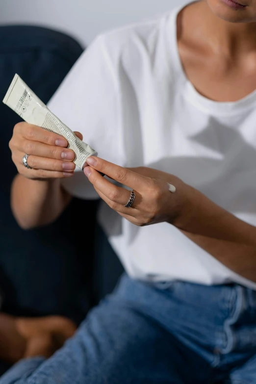 a woman sitting on a couch holding a tube of toothpaste, by Jessie Algie, pexels contest winner, zoomed view of a banknote, joints, off - white collection, soft shade