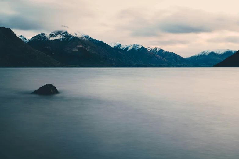 a large body of water with mountains in the background, by Sophie Pemberton, unsplash contest winner, overcast dusk, new zeeland, 4 k smooth, a cold