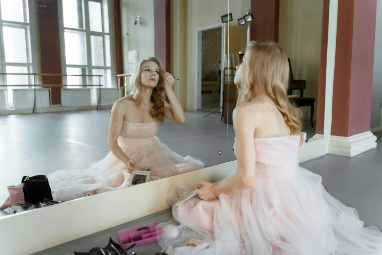 a woman in a pink dress sitting in front of a mirror, ballet style pose, putting makeup on, trending photo, filling the frame