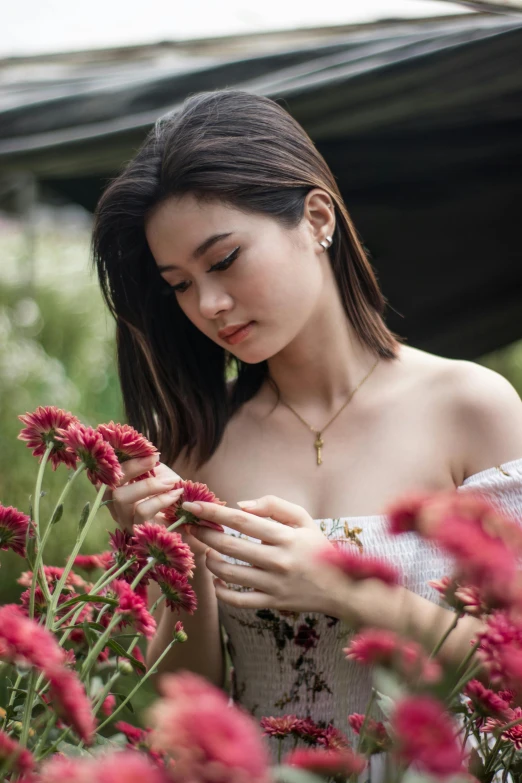 a woman standing in a field of red flowers, inspired by Ruth Jên, trending on pexels, photorealism, wearing several pendants, beautiful young asian woman, wearing elegant jewellery, sitting in the garden