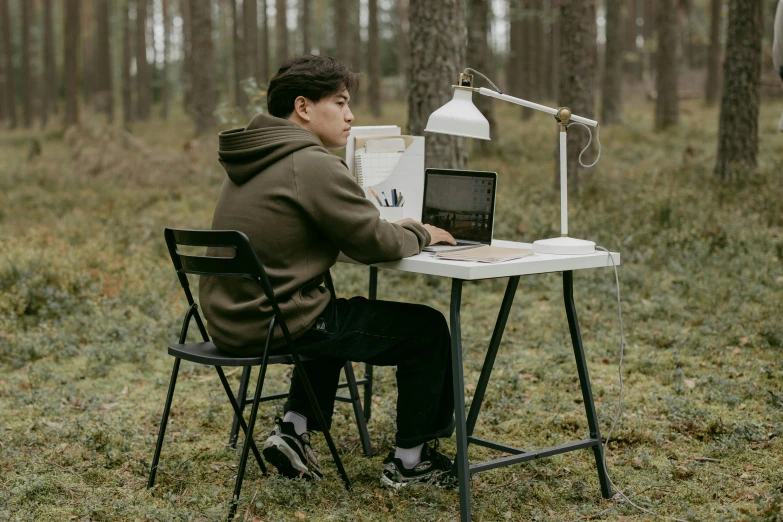 a man sitting at a table with a laptop computer, pexels contest winner, forest themed, high school, at a clearing, ignant