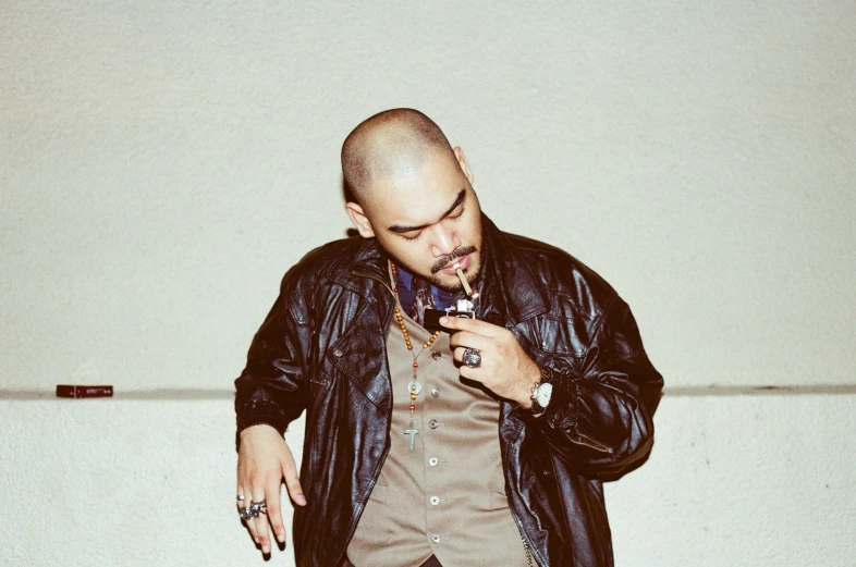 a man in a leather jacket smoking a cigarette, an album cover, inspired by Eddie Mendoza, unsplash, brown buzzcut, rapper bling jewelry, goatee, chrome hearts