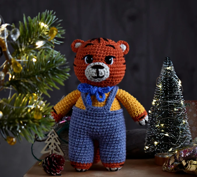 a crocheted teddy bear sitting next to a christmas tree, inspired by Ernest William Christmas, tiger, bluey, well-groomed model, warm coloured