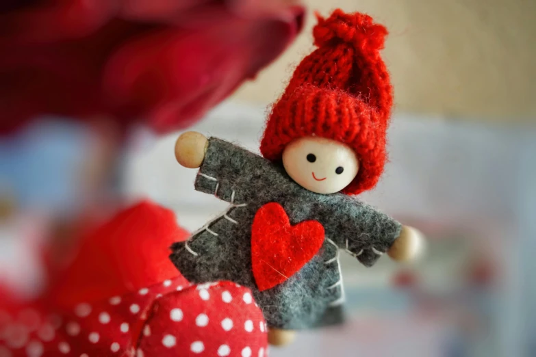 a close up of a doll holding a red heart, by Valentine Hugo, pexels contest winner, wooden decoration, red cap, red and grey only, felt