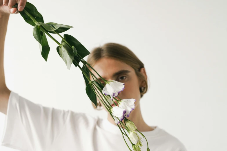 a woman holding a flower in front of her face, an album cover, inspired by Anna Füssli, aestheticism, man in white t - shirt, non binary model, ikebana white flowers, cara delevigne