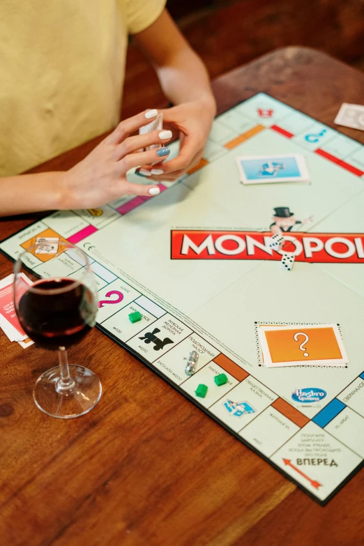 a person sitting at a table playing monopoly, enjoying a glass of wine, in-game, brown, multicoloured
