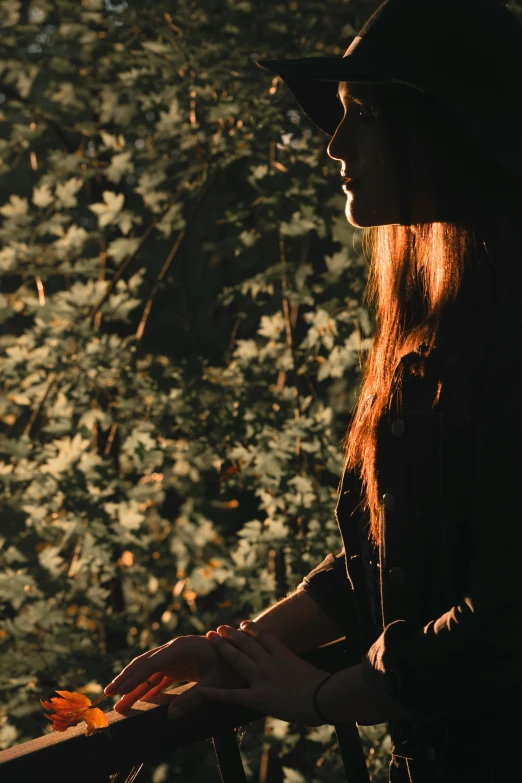 a woman in a hat standing on a balcony, inspired by Elsa Bleda, pexels contest winner, in a dark forest low light, brown red long hair, sitting under a tree, woman's profile