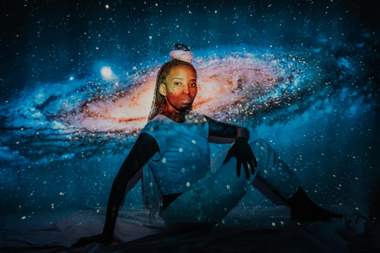a woman sitting on top of a bed in front of a galaxy, pexels contest winner, afrofuturism, in a space cadet outfit, portrait photo of a backdrop, looking towards the camera, twinkling and spiral nubela