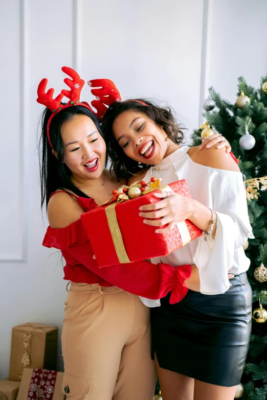 a couple of women standing next to a christmas tree, pexels contest winner, happening, holding gift, asian female, gif, both laughing