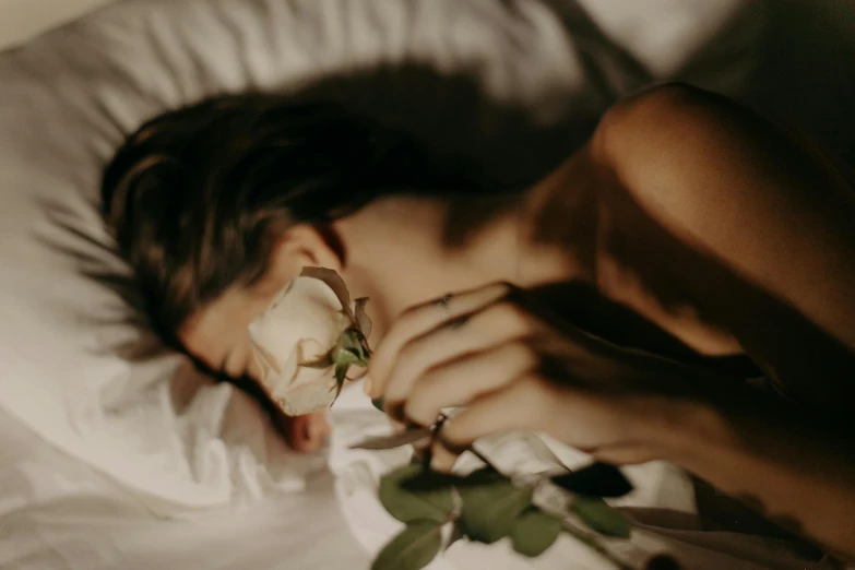 a woman laying in bed with a rose in her mouth, inspired by Elsa Bleda, trending on pexels, woman made of plants, dreamy night, with a white complexion, mournful