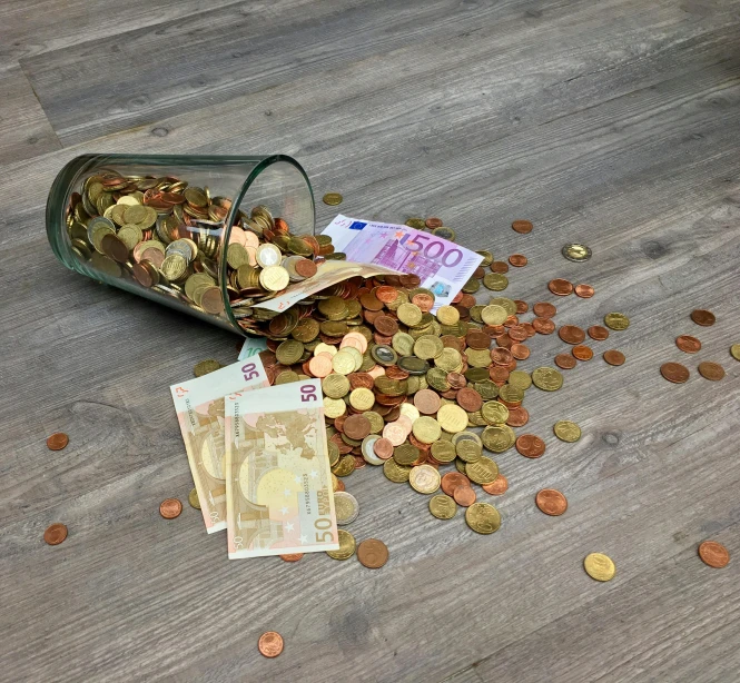 a glass filled with money sitting on top of a wooden floor