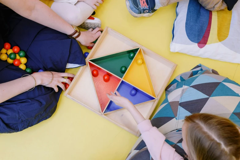 a group of people sitting on the floor playing a game, inspired by Frederick Hammersley, pexels contest winner, on a wooden tray, geodesic, primary colours, triangle