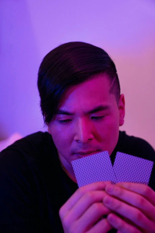 a man holding a card in front of his face, by Robbie Trevino, pexels contest winner, magical realism, purple ambient light, 8 0 s asian neon movie still, playing cards, lgbtq