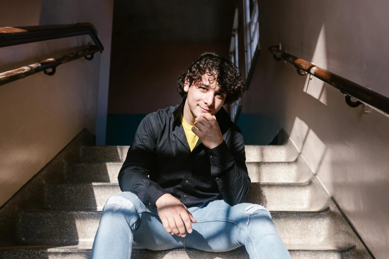 a young man sitting on a set of stairs, pexels contest winner, curly haired, shabab alizadeh, avatar image, at college