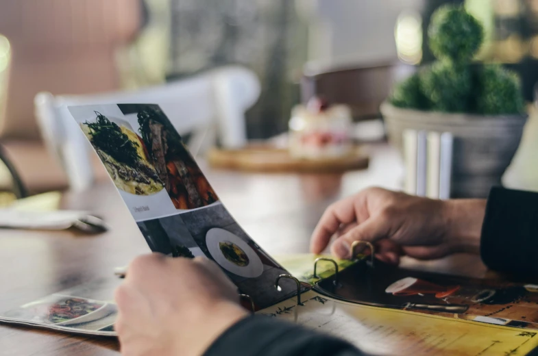 a person sitting at a table with a book open, a picture, pexels contest winner, 9 9 designs, restaurant menu photo, tabletop gaming, thumbnail