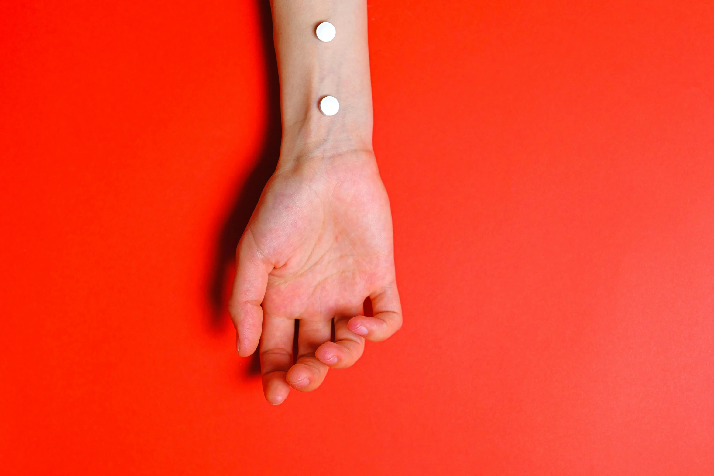 a close up of a person's wrist on a red background, an album cover, inspired by Damien Hirst, trending on pexels, hyperrealism, acupuncture treatment, magnetic, full body image, white paled skin