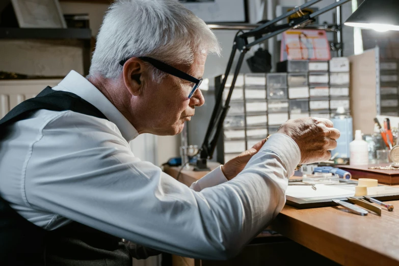 a man sitting at a desk working on a piece of wood, by Jay Hambidge, pexels contest winner, photorealism, chaumet style, wearing lab coat and glasses, david attenborough, avatar image