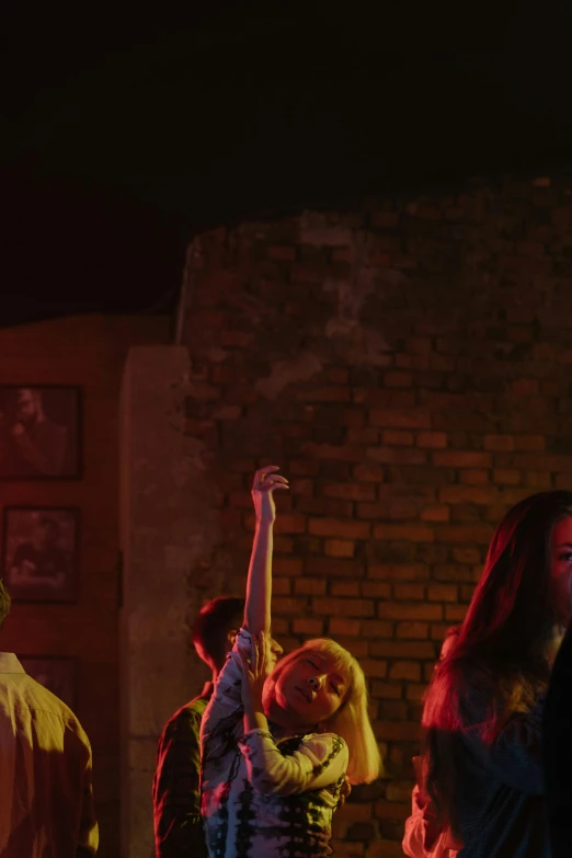 a group of people standing in front of a brick wall, happening, red and cinematic lighting, blackpink, other women dancing behind, ( ( theatrical ) )