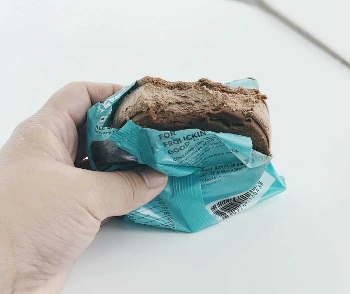 a close up of a person holding a sandwich, by Adriaen Hanneman, unsplash, chocolate candy bar packaging, brown and cyan color scheme, cracked plastic wrap, bun )