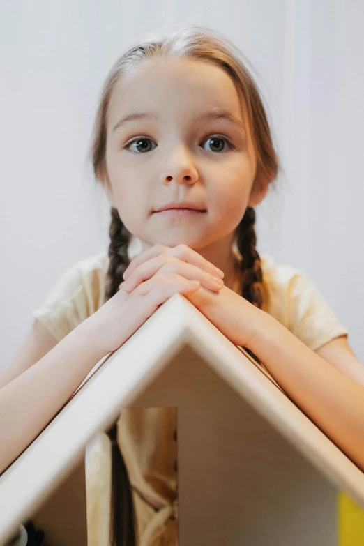 a little girl that is sitting at a table, an album cover, pexels contest winner, simple gable roofs, portrait close - up, softplay, construction