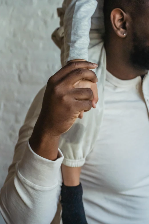 a man holding a baby on his shoulders, by Nina Hamnett, trending on unsplash, thin soft hand holding cigarette, man is with black skin, beige hoodie, close-up of thin soft hand