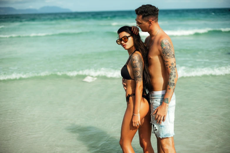 a man and a woman standing next to each other on a beach, a tattoo, hot weather, profile image, tans, 2 people