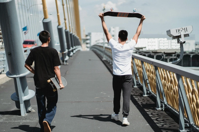 a couple of men walking across a bridge with a skateboard, pexels contest winner, happening, holding up a large shield, darren quach, aleksander rostov, sunny day time