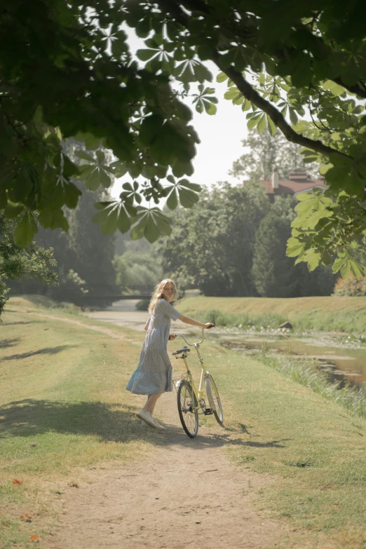 a woman standing next to a bike on a path, inspired by William Stott, visual art, still from film, parks and gardens, girl running, on a riverbank