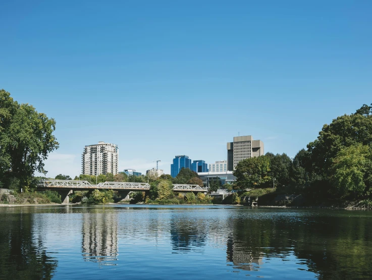 a body of water with trees and buildings in the background, a photo, inspired by Richmond Barthé, unsplash, blue river in the middle, capital city, regeneration, whistler