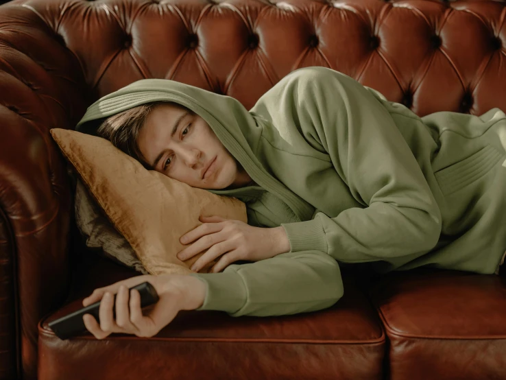 a person laying on a couch with a pillow, inspired by Balthus, trending on pexels, hyperrealism, in a hoodie, green clothes, male teenager, disappointed