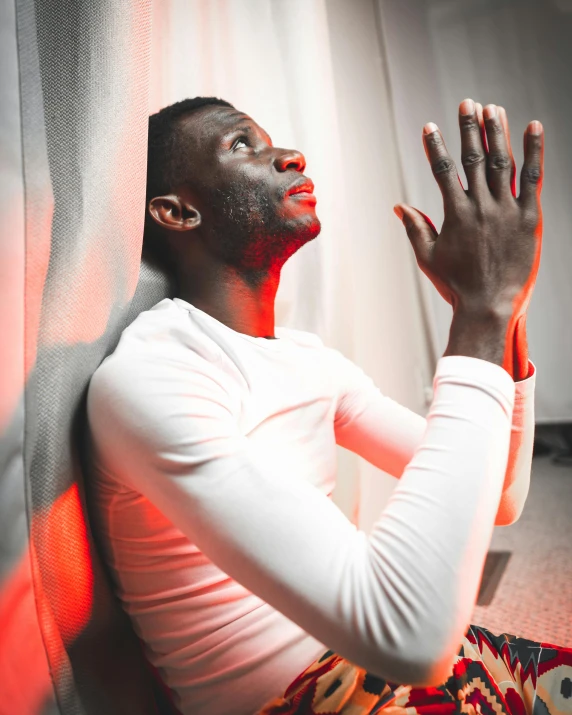 a man sitting on the floor with his hands in the air, inspired by Paul Georges, trending on pexels, light and space, patron saint of 🛸🌈👩🏾, red light from some windows, praying posture, lgbt