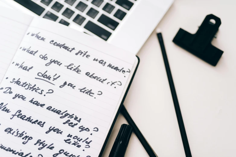 a notepad sitting on top of a desk next to a laptop, by Emma Andijewska, trending on pexels, graffiti, with some hand written letters, black eyeliner, giving an interview, incrinate content details