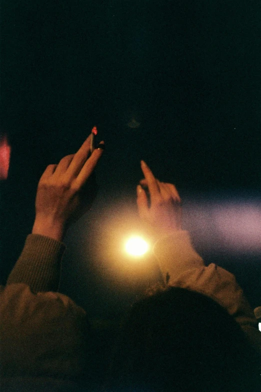 a person holding a cell phone up in the air, an album cover, inspired by Elsa Bleda, unsplash, aestheticism, candle lighting, 1 9 7 0 s analog aesthetic, holding hands in the moonlight, cigarette