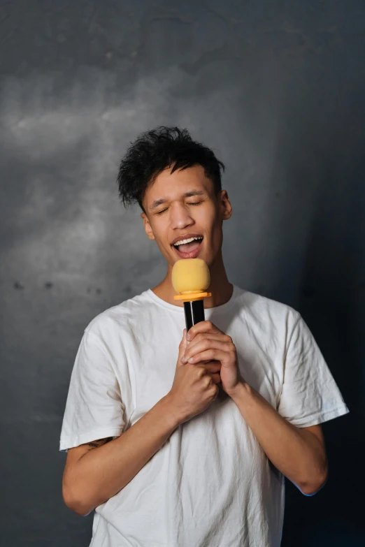 a man in a white shirt holding a microphone, inspired by Reuben Tam, pexels contest winner, non binary model, half asian, the straw is in his mouth, light skin